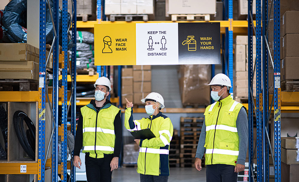 Warehouse workers in high-visibility jackets, helmets and clipboards in a warehouse