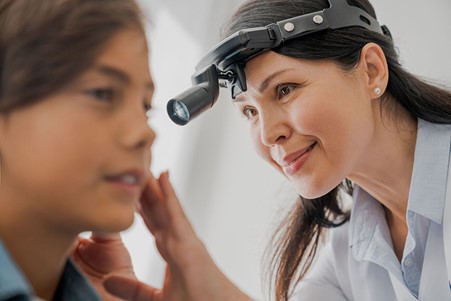 A female Otolaryngologist examining a young girls ear with a head-mounted torch